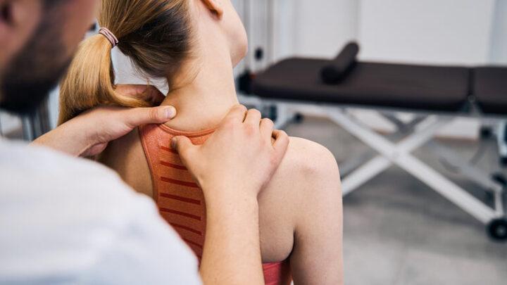 Physiotherapeut Hand massiert Frauen schmerzhaften Nacken in physischen Raum Nahaufnahme Rückenansicht. Männlicher Masseur macht Genesungstherapie nach Sportverletzung in Rehabilitationszentrum. Chiropraktische Gesundheitsversorgung