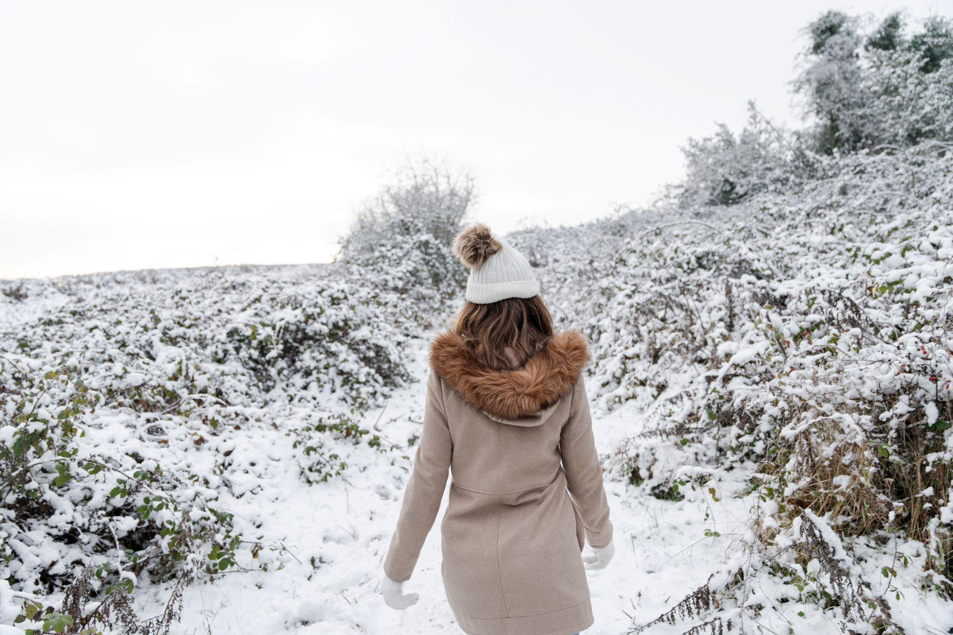 Frau mit Bommelmütze beim Winterspaziergang im Schnee