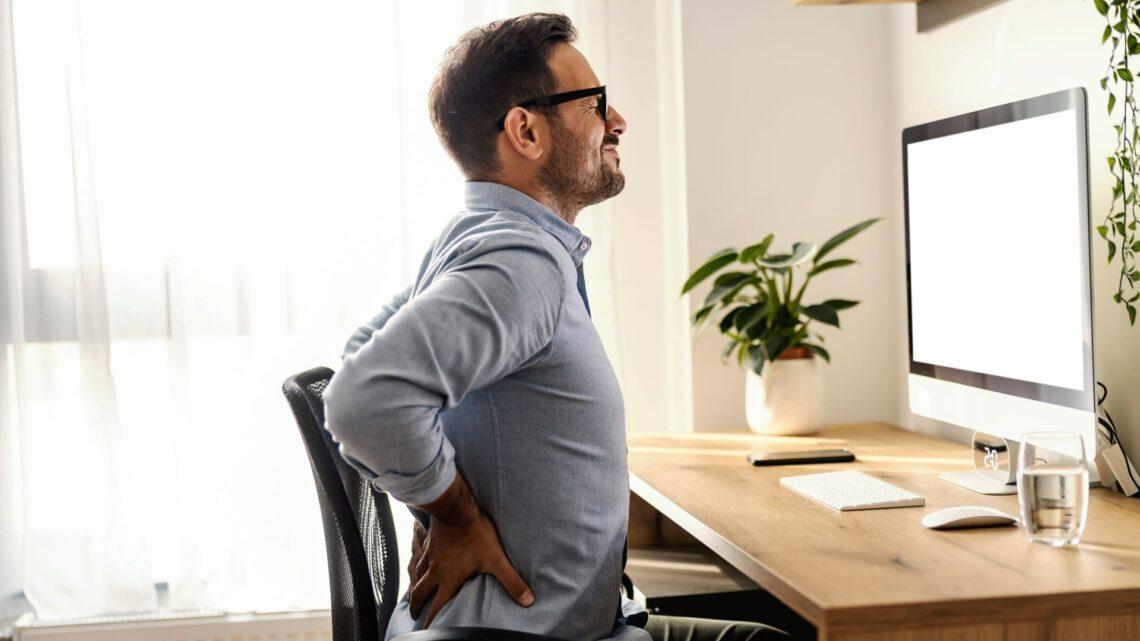 Mann mit Rückenschmerzen am Schreibtisch – Wirbelsäulentherapie Erlangen